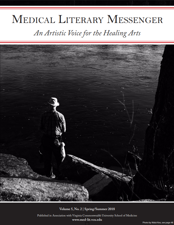 Black and white photo of a person standing on some rocks by a tree in front of a river, the MLM banner is over the top of the photo