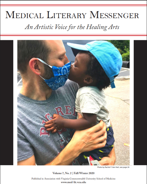 Very small child kisses his father, who is holding him and wearing a mask, the MLM banner is above the photo