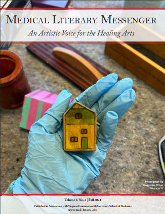 Gloved hand on a desk holding a small wooden house, the MLM banner is over the top of the photo